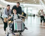 Familj på flygplatsen med ett barn sittandes på handbagage. De är glada och redo för sin resa.