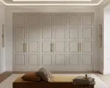 En stor garderob med klassiska paneler och guldfärgade handtag. En soffa med kuddar och en bokhylla framför. En inredning som utstrålar personlig stil.