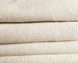 A stack of folded, natural-colored linen fabric. This image showcases the texture of linen, confirming that is linen a natural fiber.