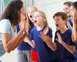 Bambini entusiasti in cerchio, con la maestra che guida attività di psicomotricità e linguaggio, stimolando espressioni vocali e corporee.