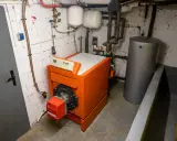 Chaudière orange vif, réservoir d'eau gris et tuyaux dans une chaufferie. Le système de chauffage fioul est prêt pour l'hiver.