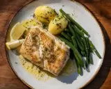 En tallrik med saftig torskrygg, kokt potatis, gröna bönor och citronklyftor. Perfekt för ett enkelt torskrygg recept.