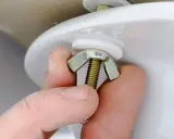 Mano ajustando tuerca mariposa para cambiar flotador cisterna.