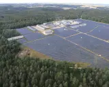 Große Solaranlage im Wald, die Sonnenenergie sammelt. Gebäude und Reihen von Solarmodulen erstrecken sich über die Landschaft.