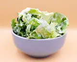 Chrupiąca sałata z jogurtem, podana w pastelowej miseczce, stanowi lekką i zdrową przekąskę.