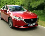 Czerwona Mazda 6 2.0 benzyna pędzi po wiejskiej drodze, otoczona zielenią drzew.