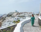 Kobieta w zwiewnej sukience spaceruje po Santorini. Idealne miejsce, gdzie do Grecji na wakacje, z widokiem na białe domy i błękitne kopuły.