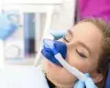 Pacjentka u dentysty z maską do podawania gazu rozweselającego. Zabieg przebiega komfortowo.