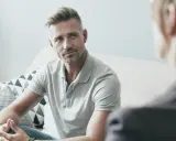 Mężczyzna w szarym polo rozmawia z terapeutą, szukając pomocy w walce z uzależnieniem od alkoholu.