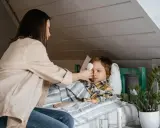 Mama mierzy gorączkę choremu dziecku, szukając domowych sposobów na zapalenie krtani u dziecka.