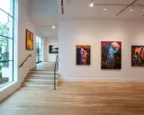 Vibrant artworks adorn the walls of Jackson Fine Art Atlanta, with a large window offering a glimpse of the lush greenery outside.