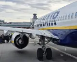 Ryanair-plan på marken med passagerare som väntar. Man undrar om man måste skriva ut boardingkort Ryanair. Flygledartorn i bakgrunden.