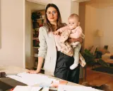 Kobieta w okularach i marynarce trzyma dziecko na rękach, przygotowując się do powrotu do pracy po macierzyńskim.