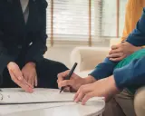 Podpisanie umowy najmu. Czy mogę wynająć mieszkanie rodziców? Dwie osoby siedzą przy stole, jedna podpisuje dokument, druga wskazuje na niego.