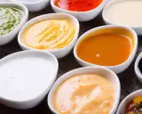 Assortiment de sauces pour raclette : verte, jaune, orange, blanche, rouge, noire. Un délice pour accompagner votre fromage fondu.