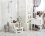 Delikatny salon w stylu shabby chic. Białe meble, ażurowa parawan, świeże kwiaty i ozdobne latarenki tworzą romantyczny nastrój.