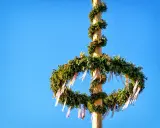 En midsommarstång i Sverige, dekorerad med grönska och band, mot en klarblå himmel.