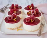 Sechs kleine Kuchen mit Himbeeren und Zitronenzesten auf einem weißen Teller.