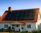 Vitt hus med solpaneler på taket. Ett takfäste med krok håller panelerna stadigt på plats.