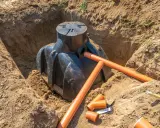 Instalacja szamba w wykopie. Pomarańczowe rury drenarskie i przyłącza czekają na montaż. Trwa praca nad tym, na jakiej głębokości drenaż odwadniający będzie skuteczny.