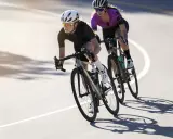Dwie kolarki w kaskach i okularach ścigają się na maratonie rowerowym. Słońce rzuca długie cienie na asfalt.