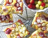 Saftiger Omas Stachelbeerkuchen, bestäubt mit Puderzucker, auf einem Gitter. Daneben eine Schale mit frischen Stachelbeeren.