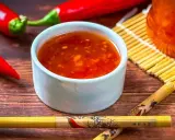 Schüssel mit leuchtend roter Sweet Chilli Sauce, daneben rote Chilis und Stäbchen. Perfekt für dein Sweet Chilli Sauce Rezept!