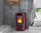 Estufa de pellets roja con fuego encendido, instalada en un salón moderno con pared de hormigón y ventana al exterior.