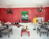 Interni di case anni '70: una donna legge sul divano bianco, un uomo mostra un quadro. Pareti rosse, lampade a grappolo.