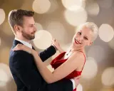 Para tańczy walca angielskiego na tle złotych bokeh. Ona w czerwonej sukni, on w garniturze.