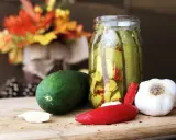 Słoik z ogórkami z chili w plastrach, obok świeży ogórek, czosnek i papryczka chili.