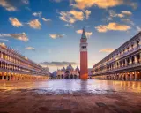 Le **place Saint-Marc à Venise** s'illumine sous un ciel de fin de journée. La basilique et le campanile se dressent majestueusement.
