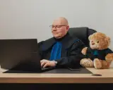 Prawnik w todze z pluszowym misiem obok, pracujący przy laptopie. Zastanawiasz się, ile kosztuje porada prawna?