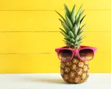 Ananas w okularach przeciwsłonecznych na żółtym tle. Czy wiesz, jaki ananas indeks glikemiczny ma dla Twojej diety?