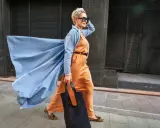 Elegancka kobieta w pomarańczowym garniturze i błękitnym płaszczu z wiatrem we włosach. Inspiracja dla mody dla starszych panów.