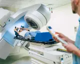 Ragazza sdraiata su lettino per radioterapia, tecnico in primo piano controlla il macchinario. Speranza di guarigione, ma con il timore dei radioterapia danni permanenti.
