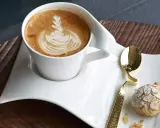 Ein Latte Macchiato mit schönem Milchschaum-Muster und ein Mandelgebäck, perfekt zum wiener Zubereiten.