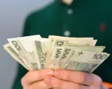 Dłonie trzymają wachlarz banknotów 100 zł. Może to być pomoc finansowa, np. renta po zmarłym ojcu, która zapewnia wsparcie.