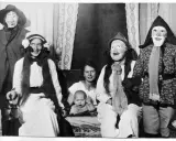 En familj klädd i masker och dräkter, kanske en del av julens historia, poserar för ett fotografi. En bebis sitter i förgrunden.