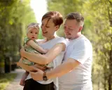 Szczęśliwa rodzina z córeczką w letnim parku. Mama tuli dziecko, tata obejmuje ich. Idealne babciowe warunki na spacer.