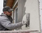 Budowlaniec nakłada tynk silikatowo silikonowy na elewację, używając kielni. Siatka zbrojeniowa jest widoczna pod świeżą warstwą.