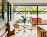 Sedie in paglia e metallo, ispirate a Marcel Breuer, attorno a un tavolo di vetro in una luminosa sala da pranzo con vista sul giardino.