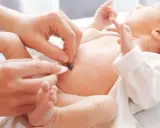 Delikatne czyszczenie kikuta pępowiny noworodka. Dłoń rodzica ostrożnie dotyka małego brzuszka, by zadbać o higienę.