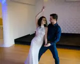 Para tańczy w białej sukni i granatowym garniturze. Ich ruchy są płynne, jakby tworzyli idealny, taneczny duet.