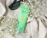 Zielona tubka z filtrem przeciwsłonecznym SPF 50 z aloesem, otoczona delikatnymi białymi kwiatami i okularami przeciwsłonecznymi.