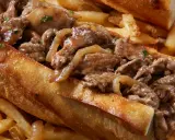 Un delicioso pepito de ternera jugoso, relleno de tiernos trozos de carne y cebolla caramelizada, acompañado de crujientes patatas fritas.