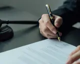 Sądowy młotek i dłoń pisząca dokument. Sprawa dotyczy wydziedziczenia a zachowku.