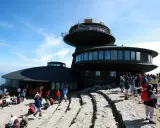 Ludzie odpoczywają na kamienistym szlaku na Śnieżkę, podziwiając widok na budynek obserwatorium.