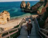 Persona desciende escaleras de madera hacia una hermosa playa de lagos con formaciones rocosas y aguas turquesas.