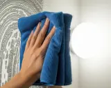 Hand putzt Spiegel mit blauem Mikrofasertuch. Perfekt für welche Lappen zum Bad putzen.